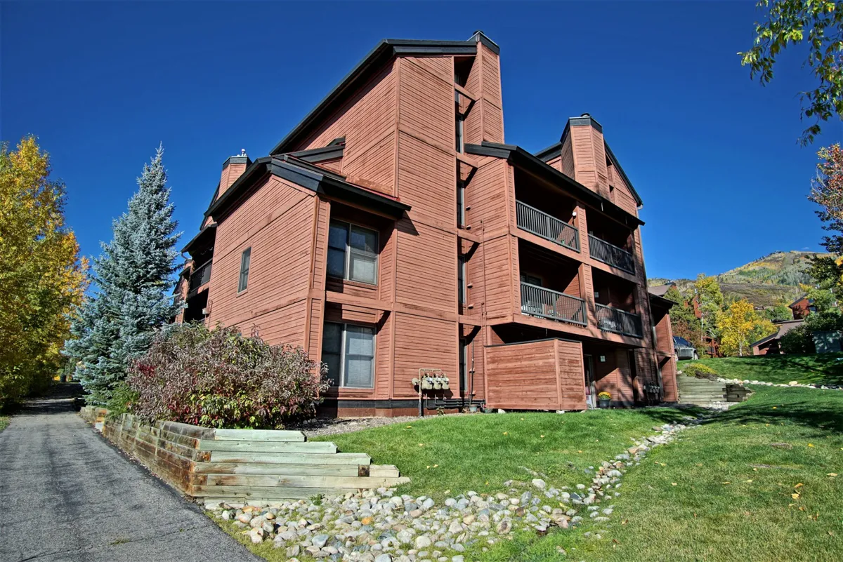 The exterior of Timber Run features warm wooden architecture, balconies with railings, a manicured green lawn, and mature trees, conveying the inviting and tranquil environment of the property. The view hints at opportunities for outdoor gatherings, morning coffee on the balcony, and easy access to surrounding trails.