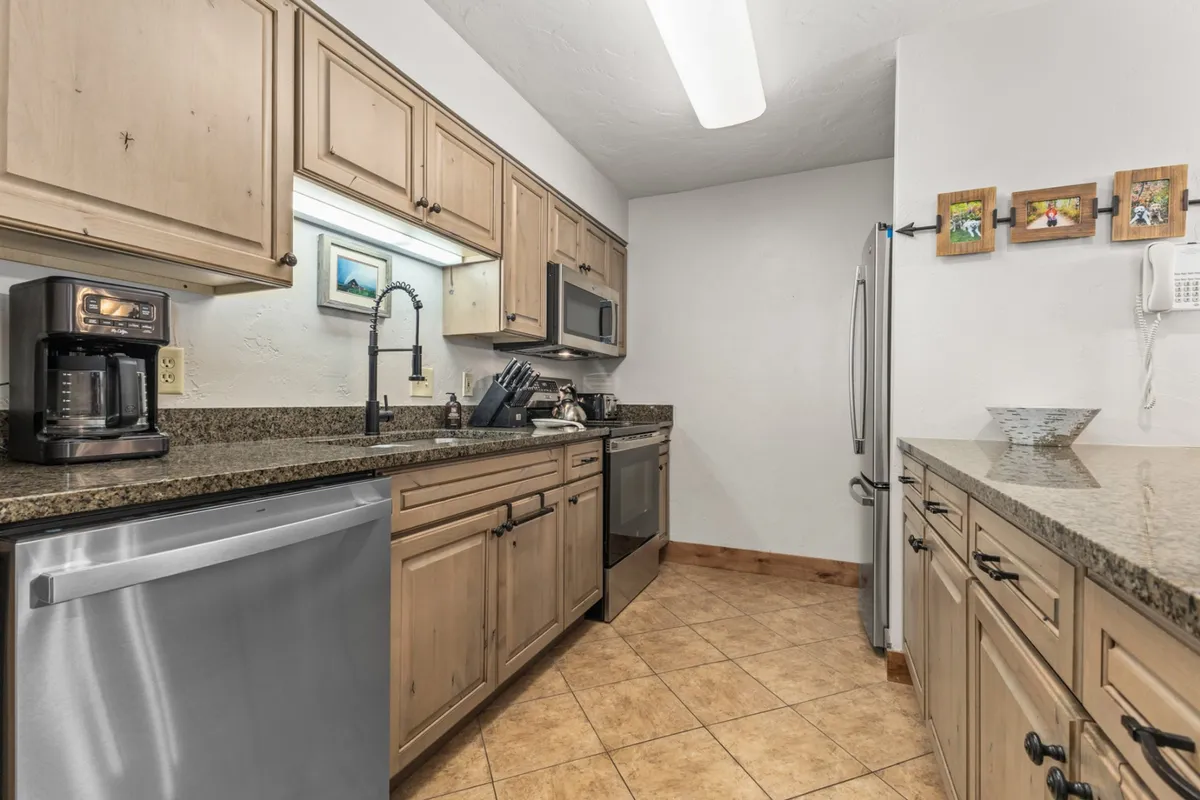 A view of the kitchen area with granite countertops, stainless steel appliances, wooden cabinetry, and a coffee maker, creating a functional yet inviting space for meal preparation and casual gatherings at the breakfast bar.