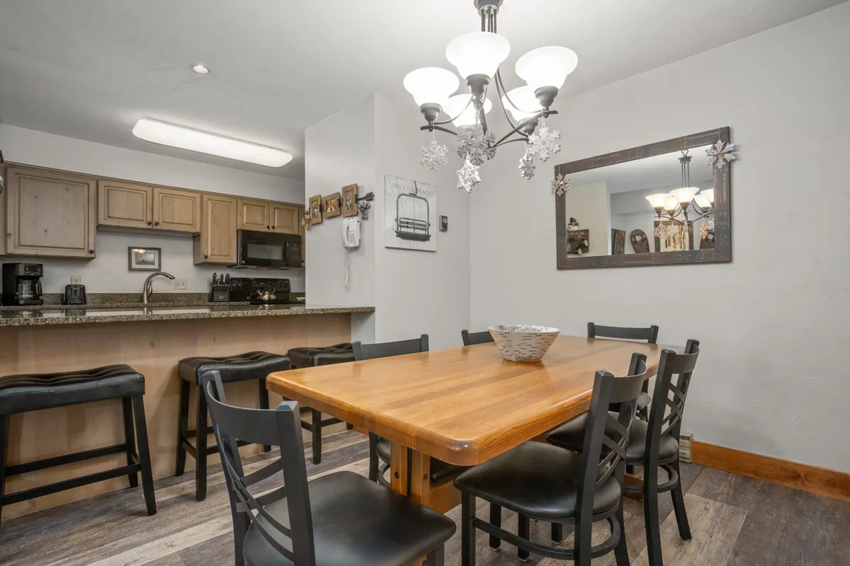 A dining area with a table that seats six beneath a warm chandelier, adjacent to the kitchen counter. The setting is welcoming and ideal for group meals or board game nights, capturing the spirit of togetherness emphasized in the narrative.