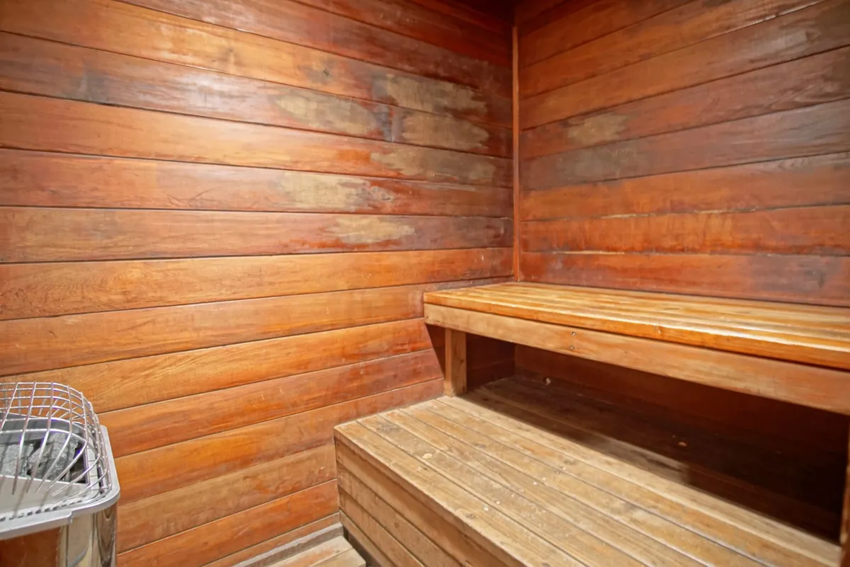 A warm, inviting interior shot of a wooden sauna, complete with benches and a central heating element. The space is serene and designed for relaxation and wellness routines.