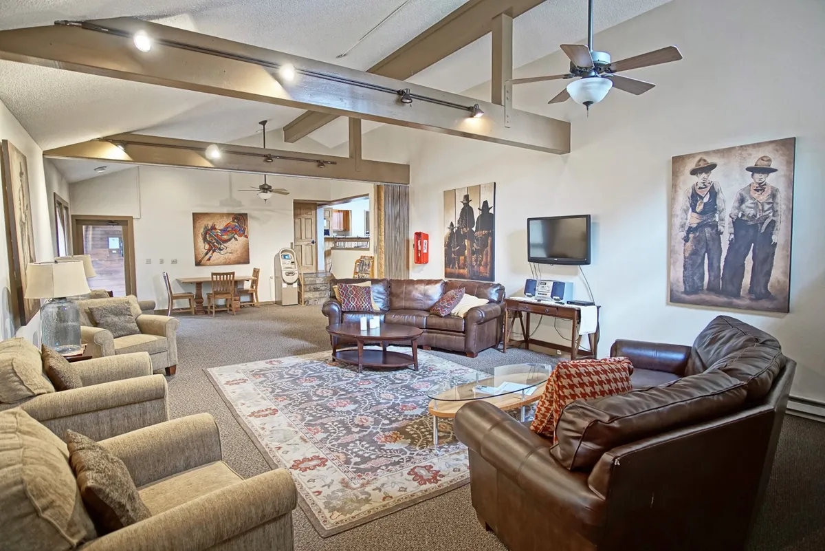 A comfortable, spacious lobby or common area with large fabric sofas, artwork on the walls, wooden beams, a coffee table, and a cozy rug. The seating arrangement fosters both relaxation and social interactions, hinting at a welcoming space where guests may interact with concierge staff.