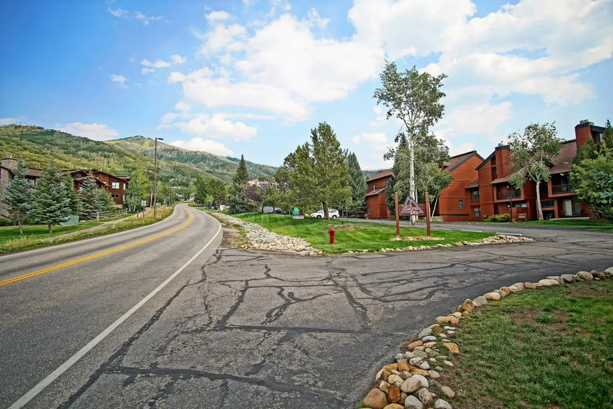 This image captures a winding road set against a picturesque mountain backdrop, with townhouses and lush greenery framing the scene. Hints of community life are visible, including pathways and a fire hydrant, suggesting ease of exploration and access to nearby attractions.