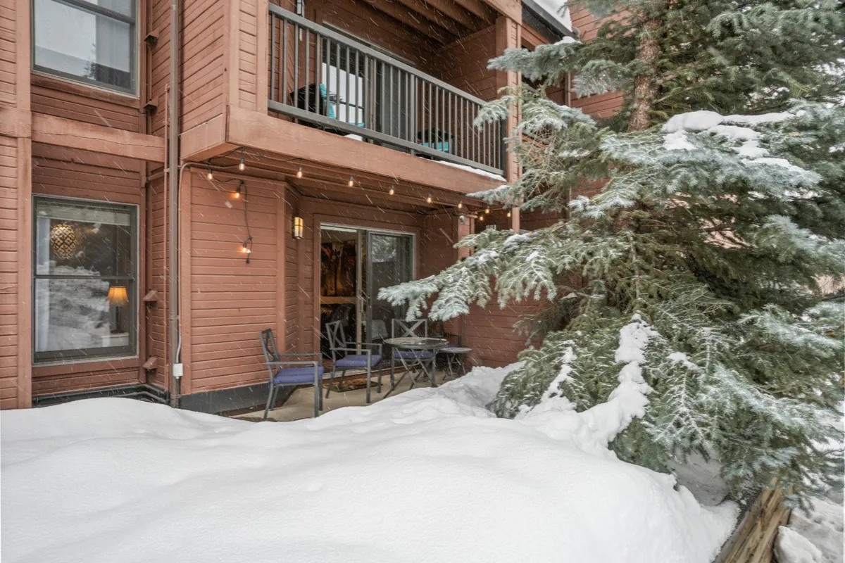 A wooden balcony overlooking a snow-covered ground, strung with twinkling lights and arranged with cozy seating. The scene radiates warmth and comfort, ideal for gathering with friends or family amidst a wintry backdrop.