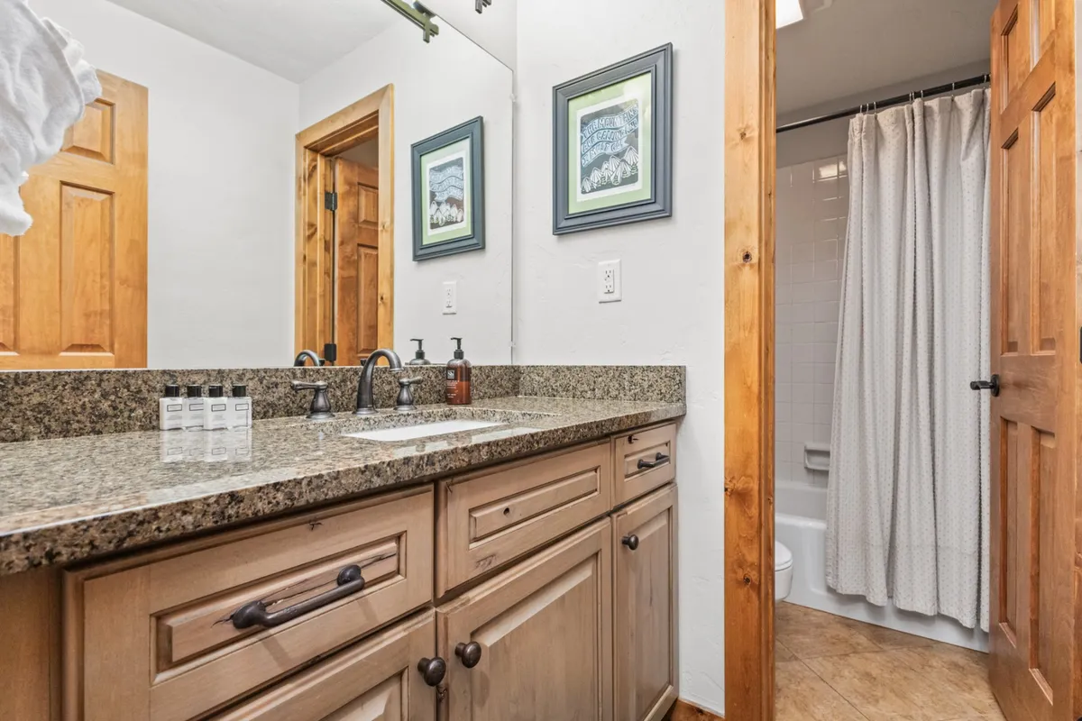 A stylish bathroom with a dual sink vanity, textured granite countertop, rich wooden cabinetry, and decorative wall art. The spacious layout and quality finishes invite relaxing morning and evening routines.